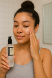 A young woman applying COSRX Advanced Snail 96 Mucin Power Essence to her face, promoting hydrated, glowing skin in a clean bathroom setting.